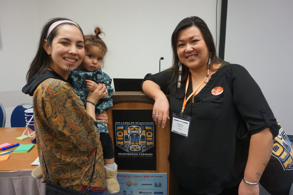 Annauk Olin, holding her daugher Tulġuna T'aas Olin, and Rochelle Adams pose on March 20, 2024, after giving a presentation on language at the Alaska Just Transition Summit in Juneau. (Photo by Yereth Rosen/Alaska Beacon)