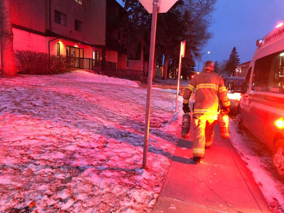 A Calgary firefighter carries two oxygen tanks outside a building where one body was found in a suite after a fire. (Colleen Underwood/CBC - image credit)