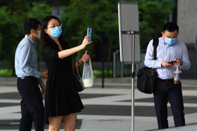 SINGAPORE - JUNE 12: A woman wearing protective masks scans a Safe Entry QR code before entering a bank on June 12, 2020 in Singapore. From June 2, Singapore embarked on phase one of a three phase approach against the coronavirus (COVID-19) pandemic as it began to ease the partial lockdown measures by allowing the safe re-opening of economic activities which do not pose high risk of transmission. This include the resumption of selected health services, re-opening of schools with school children attending schools on rotational basis, manufacturing and production facilities, construction sites that adhere to safety measures, finance and information services that do not require interactions and places of worship, amongst others. Retail outlets, social and entertainment activities will remain closed and dining in at food and beverage outlets will still be disallowed. The government will decide further to ease restriction by the middle of June if the infection rate within the community remains low.  (Photo by Suhaimi Abdullah/Getty Images)