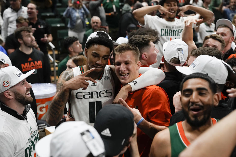 Miami guard Jordan Miller (11) poses for a picture with a fan, as teammates celebrate defeating Pittsburgh in an NCAA college basketball game, to win a share of the Atlantic Coast Conference regular season championship with Virginia on Saturday, March 4, 2023, in Coral Gables, Fla. (AP Photo/Rebecca Blackwell)