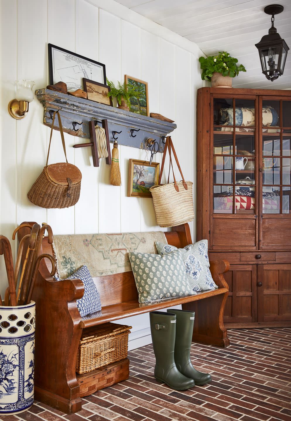 collected entryway with antique wooden bench, umbrella stand full of walking sticks, antique peg rail with baskets, bags, and other misc antiques