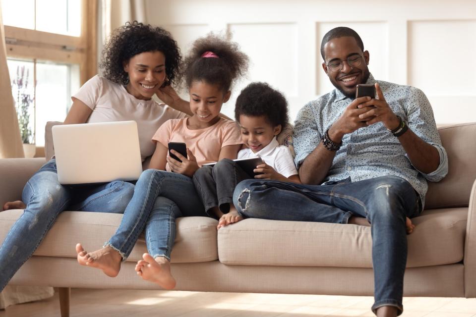 A family of four seated on a couch, each of which is engaged with their own wireless device.