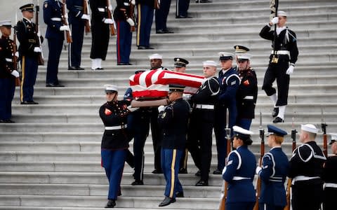 The flag-draped casket of former President George HW Bush is carried by a joint services military honor guard  - Credit: AP