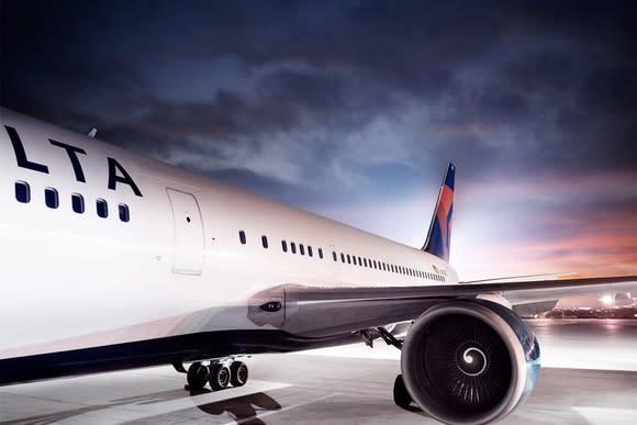 White airplane with Delta markings on a clean tarmac under a dark overcast sky near sunset.