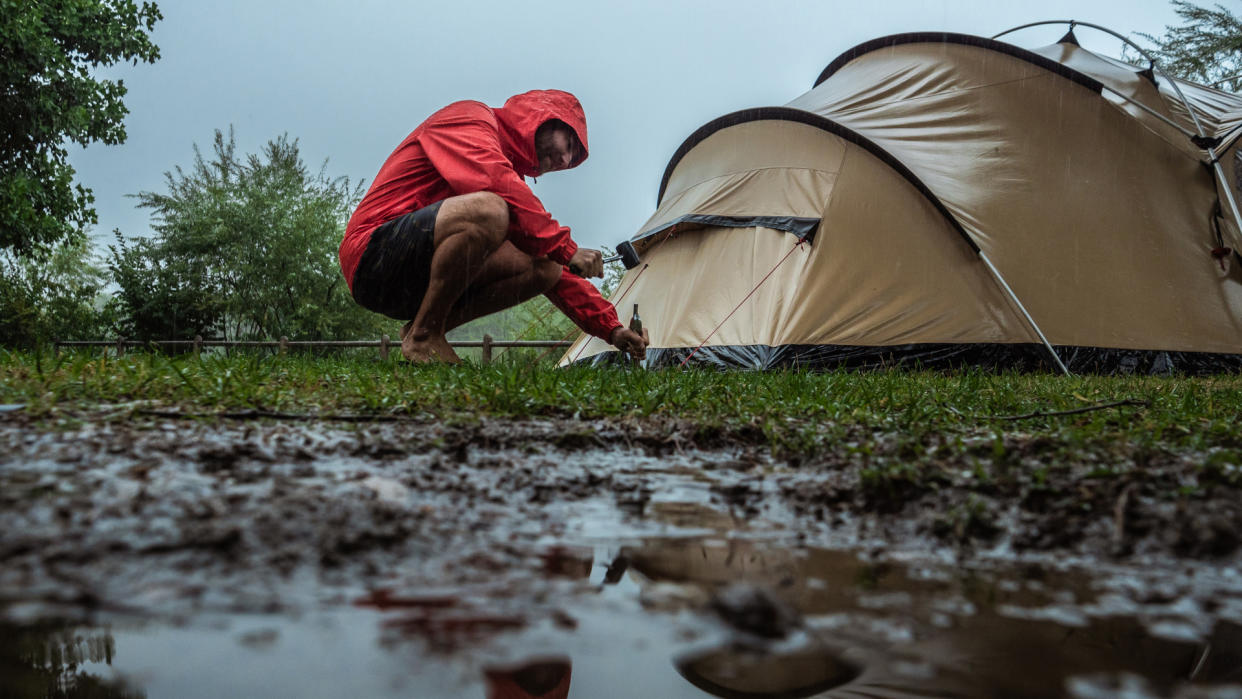  How to camp in the rain: a man setting up his tent in the rain. 