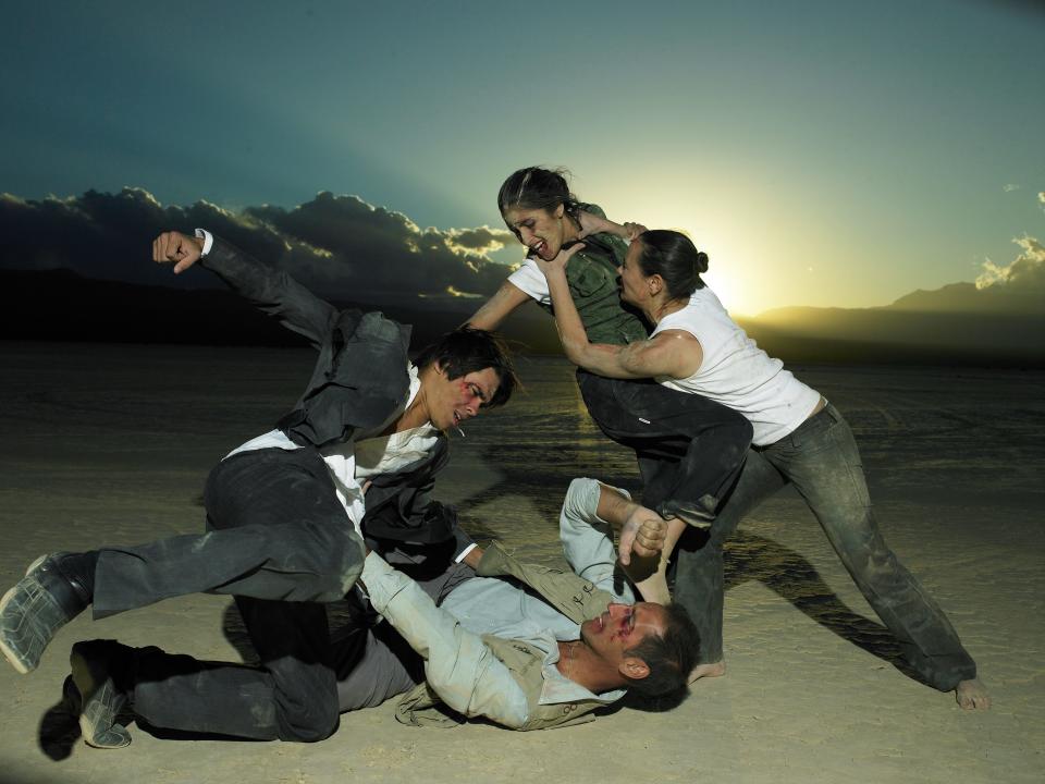 A group of four people dressed in business attire fighting in desert at dusk.