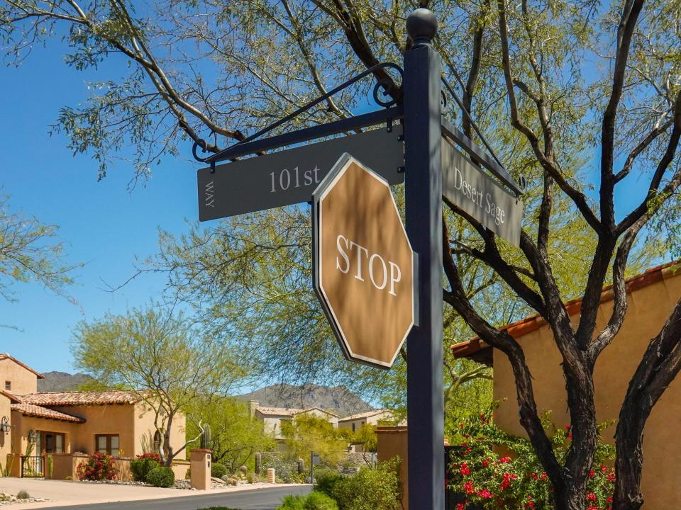 A fancy-looking street sign in a neighborhood lined with an adobe house surrounded by mountains.