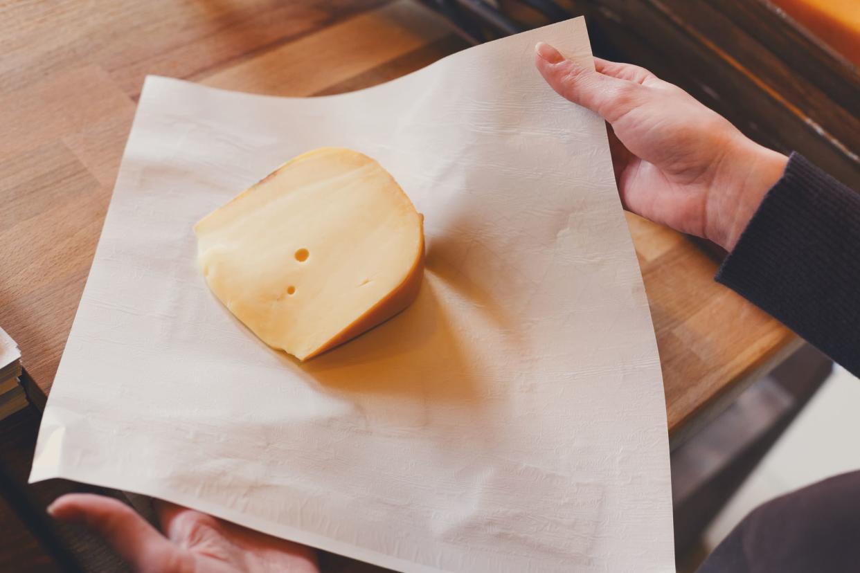 Female shop assistant wrapping a piece of radamer cheese on wooden table, copy space