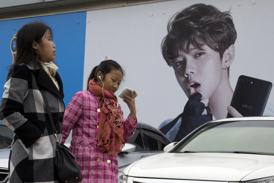 FILE - In this Oct. 21, 2017, file photo, Chinese women walk past advertisement featuring teen idol Lu Han, also known as China's Justin Bieber in Beijing. China's government banned effeminate men on TV and told broadcasters Thursday, Sept. 2, 2021 to promote "revolutionary culture," broadening a campaign to tighten control over business and society and enforce official morality. (AP Photo/Ng Han Guan, File)