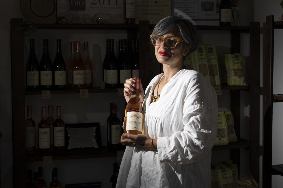 Rosanna Picoco, a volunteer for Libera, an association against Mafia and criminal organisations, poses during an interview in one of the association shop in Mesagne, Italy, Monday, May 20, 2024. Picoco shows a bottle of a wine dedicated to Marcella di Levrano a young woman killed by Sacra Corona Unita in 1990. As a child bombs were left in her school overnight by the SCU as a threat to local store owners who had children in the school and were refusing to pay of the local mafia. All the parents agreed they would bring their children to school the next day as though nothing had happened. This instilled in her the idea that citizens have to be active and participate in opposing the mafia, not just quietly turn away. (AP Photo/Alessandra Tarantino)