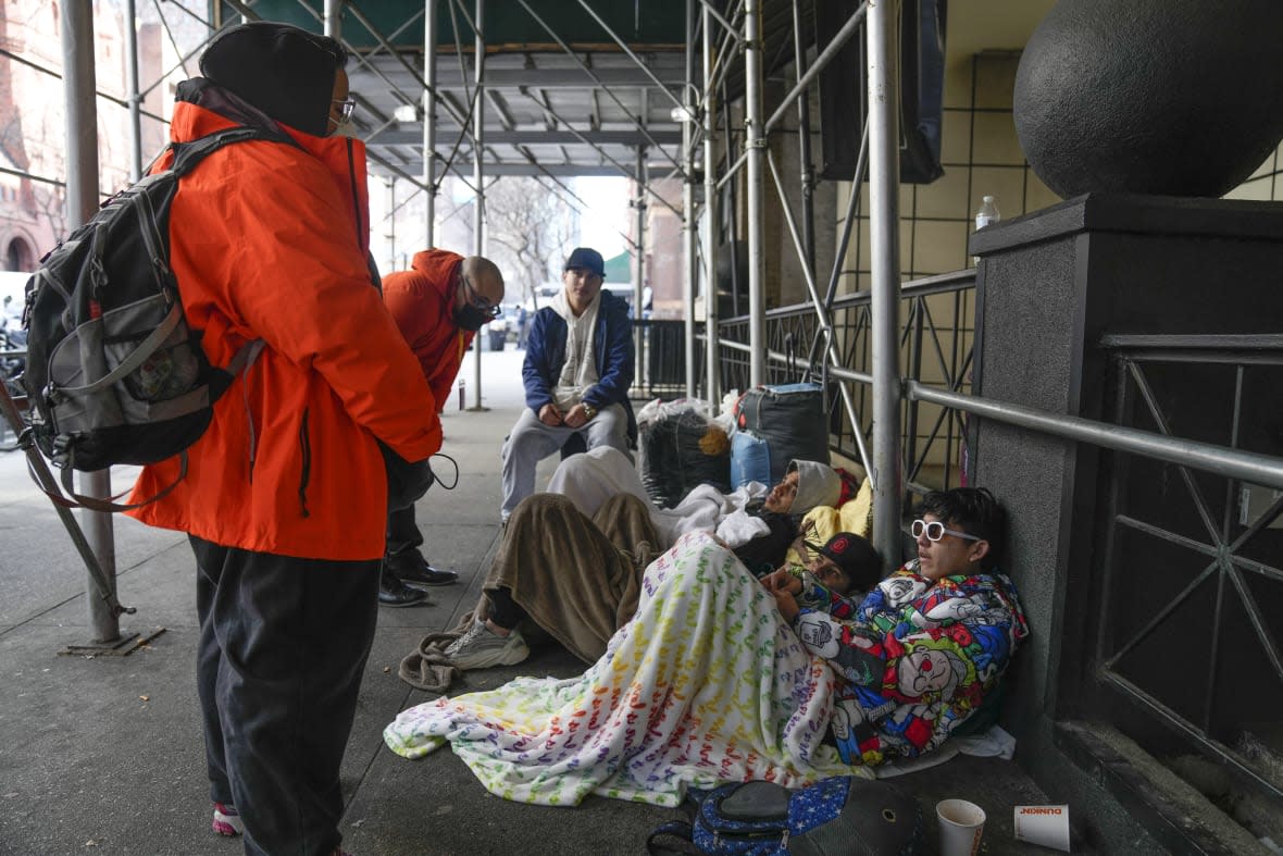 Recent immigrants to the United States lie on the sidewalk with their belongings as they talk to city officials in front of the Watson Hotel in New York, Monday, Jan. 30, 2023. (AP Photo/Seth Wenig, File)