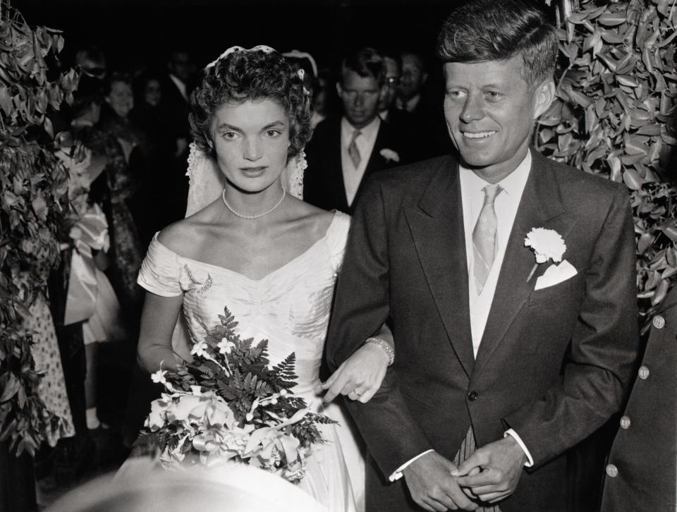 Jacqueline Lee Bouvier, holding a bouquet, walks arm-in-arm with John F. Kennedy Jr.