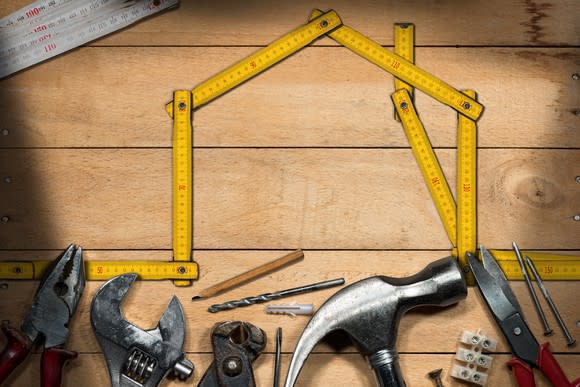 Home-improvement tools lined up under a yellow measuring tape shaped like the outline of a house.