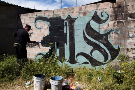 FILE PHOTO: A police officer paints over a graffiti associated with the Mara Salvatrucha gang in the Montreal neighborhood in Mejicanos, El Salvador December 9, 2015. REUTERS/Jose Cabezas/File Photo