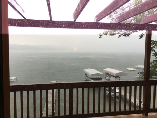 View from a covered deck showing lightning striking over a lake with boats and docks