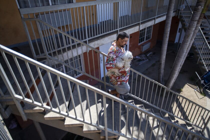 Downey, CA - June 30: Mario Blanco, walks down steps carrying his dog, "Leo the Lion," at Chateau Inn & Suites on Thursday, June 30, 2022, in Downey, CA. It was Thursday morning, June 30, moving day for 53-year-old Blanco and other unhoused tenants of the Chateau Inn & Suites in Downey, the place they've called home for a year. (Francine Orr / Los Angeles Times)