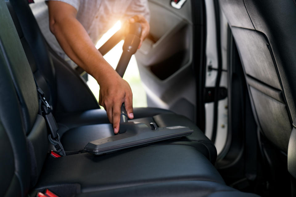 A stock photo shows a man cleaning the backseats of a car with a vacuum cleaner.