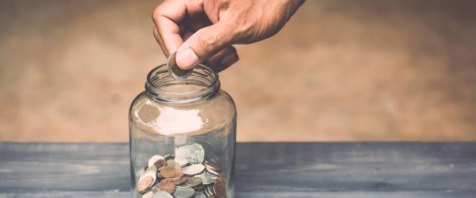 hand drops money into a glass jar for a savings