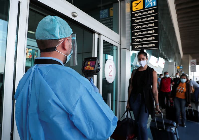 A healthcare worker measures the temperatures of travelers before entering the Tocumen International Airport during the coronavirus disease (COVID-19) outbreak, in Panama City