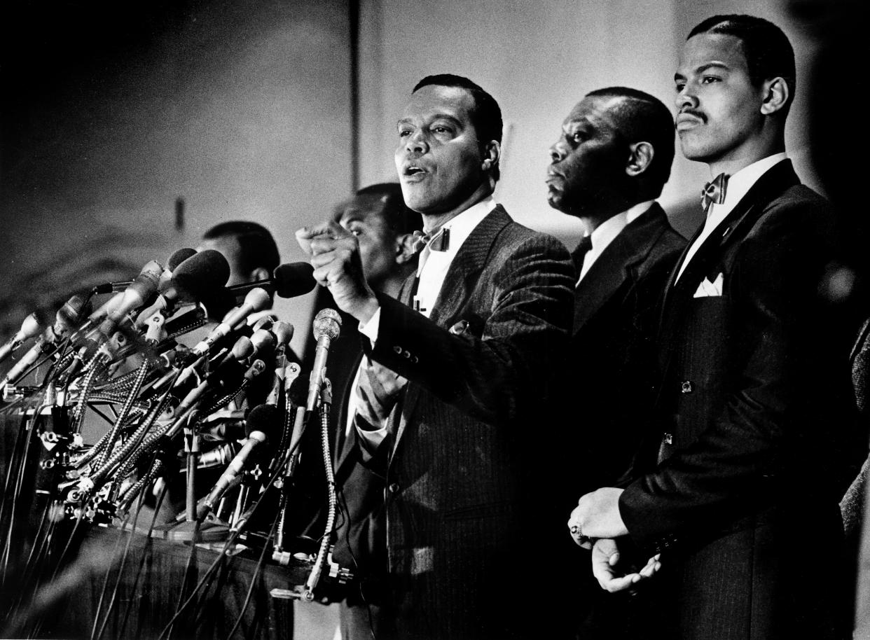 Louis Farrakhan at the microphone, surrounded by followers also wearing bowties, suits and starched white shirts.