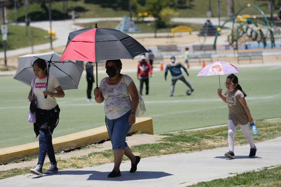 Visitors cover themselves from the heat with umbrellas as temperatures rise at MacArthur Park, Tuesday, July 11, 2023, in Los Angeles. (AP Photo/Marcio Jose Sanchez)