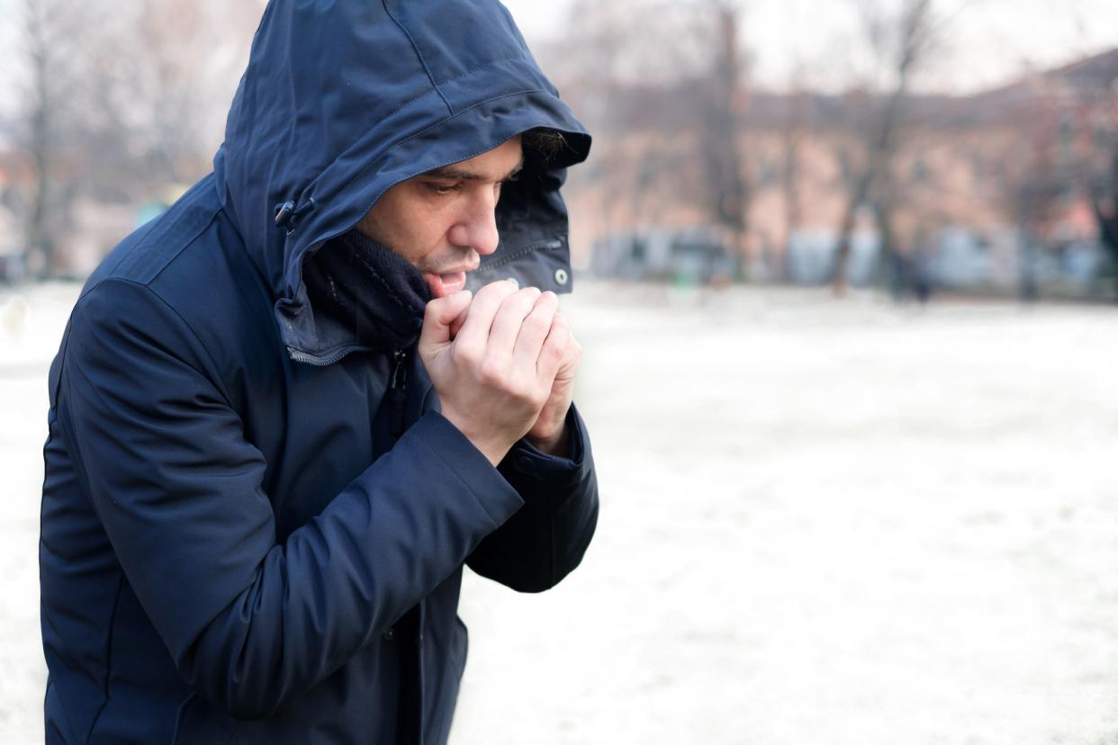 man in coat breathes into his hands, cold