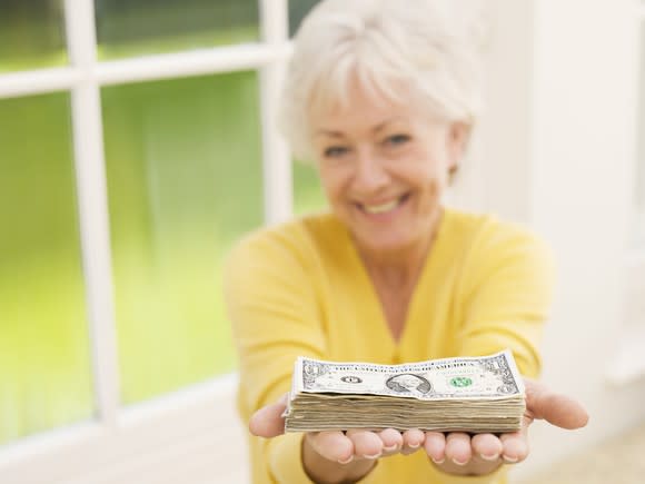 A senior woman holding out a neat stack of cash bills.