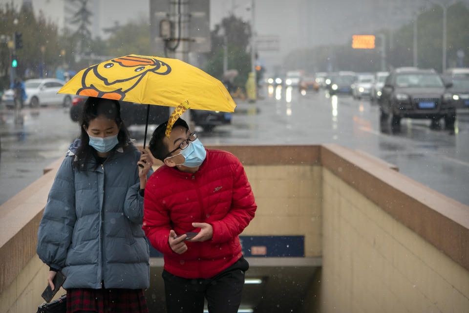 People wearing face masks to protect against the coronavirus hold an umbrella as they walk through the first snowfall of the season in Beijing, Saturday, Nov. 21, 2020. China is starting mass testing on 3 million people in a section of the northern city of Tianjin and has tested thousands of others in a hospital in Shanghai after the discovery of a pair of cases there. (AP Photo/Mark Schiefelbein)