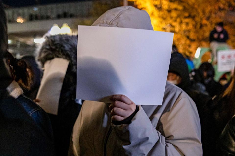 Demonstrators hold sheets of blank white paper in front of their faces