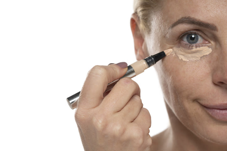 A person applying concealer under their eye with a makeup stick