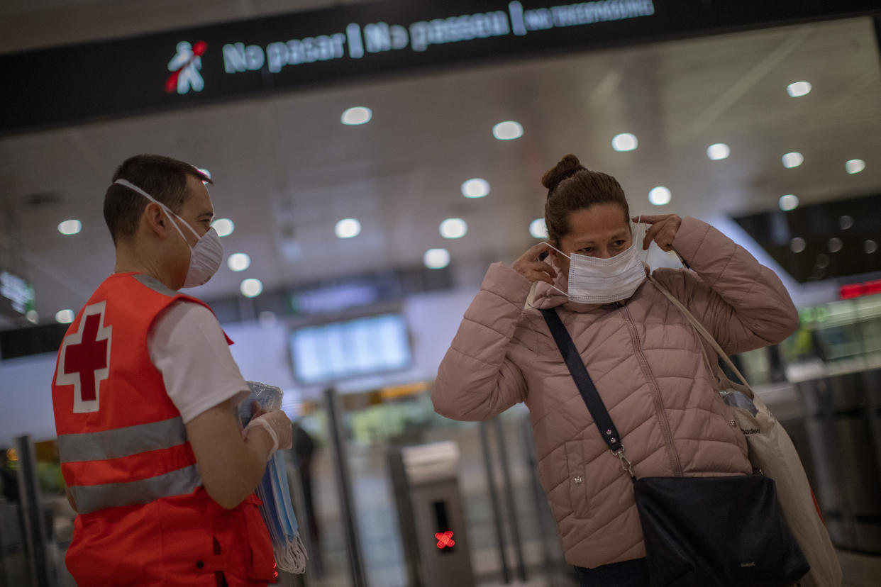 Una mujer recibe una mascarilla distribuida por un voluntario de Cruz Roja la principal estación de tren de Barcelona, el 14 de abril de 2020. (AP Foto/Emilio Morenatti)