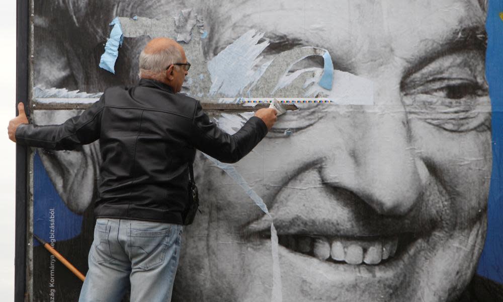 An activist removes a government billboard in Budapest showing George Soros next to a message that he plans to settle a million migrants in Europe per year.