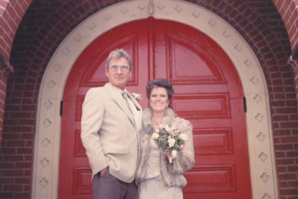 Couple standing at a church entrance, man in suit and woman holding flowers