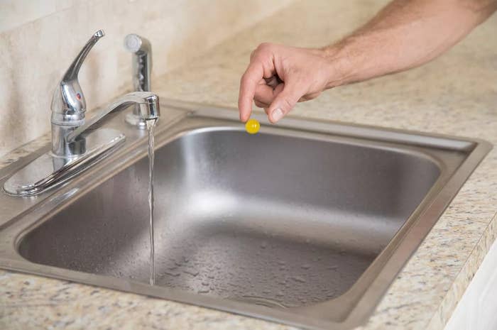 a hand dropping the yellow, marble-sized ball into the sink