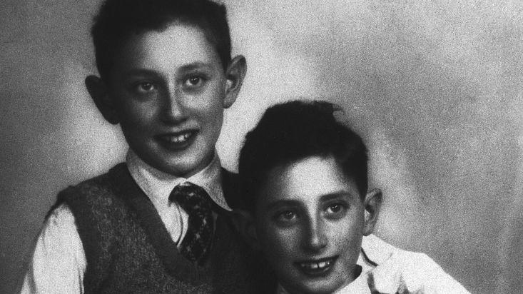 henry kissinger stands behind brother walter kissinger as both boys smiles for a photo, they wear matching collared shirts, ties, and sweater vests