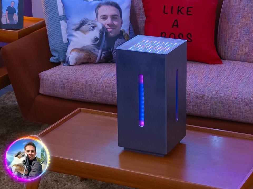 a black computer tower with blue and pink lights on it, sitting on a coffee table. behind it, there's a couch and throw pillows with Max's face on them, and captions like "like a boss"