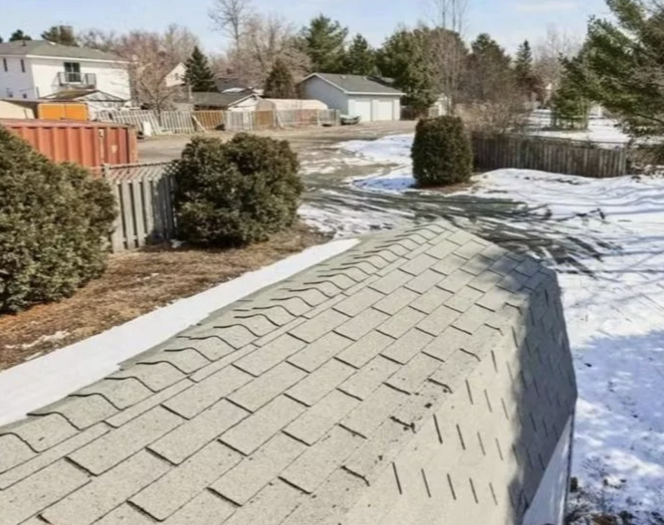 Driveway with snow on the sides leading to a house, partial view of neighboring houses and trees