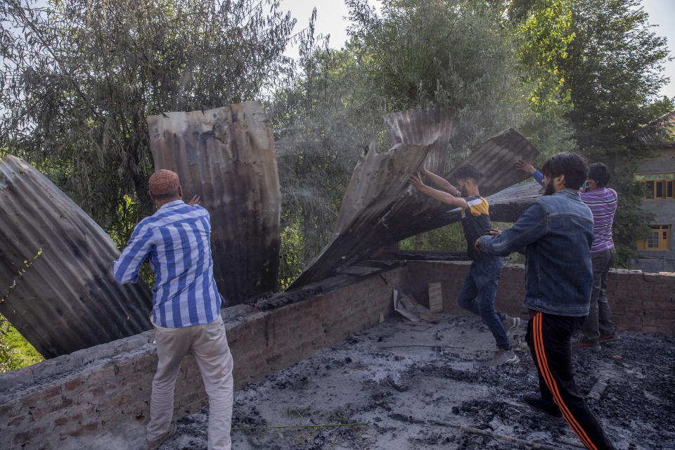 Kashmiris push damaged tin roof as they clear the house damaged in a gun battle on the outskirts of Srinagar, Indian controlled Kashmir, Tuesday, June 29, 2021. Hours after arresting a rebel commander, police Tuesday said he was killed during a crossfire with another militant in the disputed city's region's main city. (AP Photo/Dar Yasin)