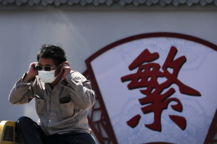 A man puts on his face mask to protect against the new coronavirus as he sits on a tricycle cart passing by the words "Complicated" on a street in Beijing, Tuesday, Aug. 4, 2020. Both mainland China and Hong Kong reported fewer new cases of COVID-19 on Tuesday as strict measures to contain new infections appear to be taking effect. (AP Photo/Andy Wong)