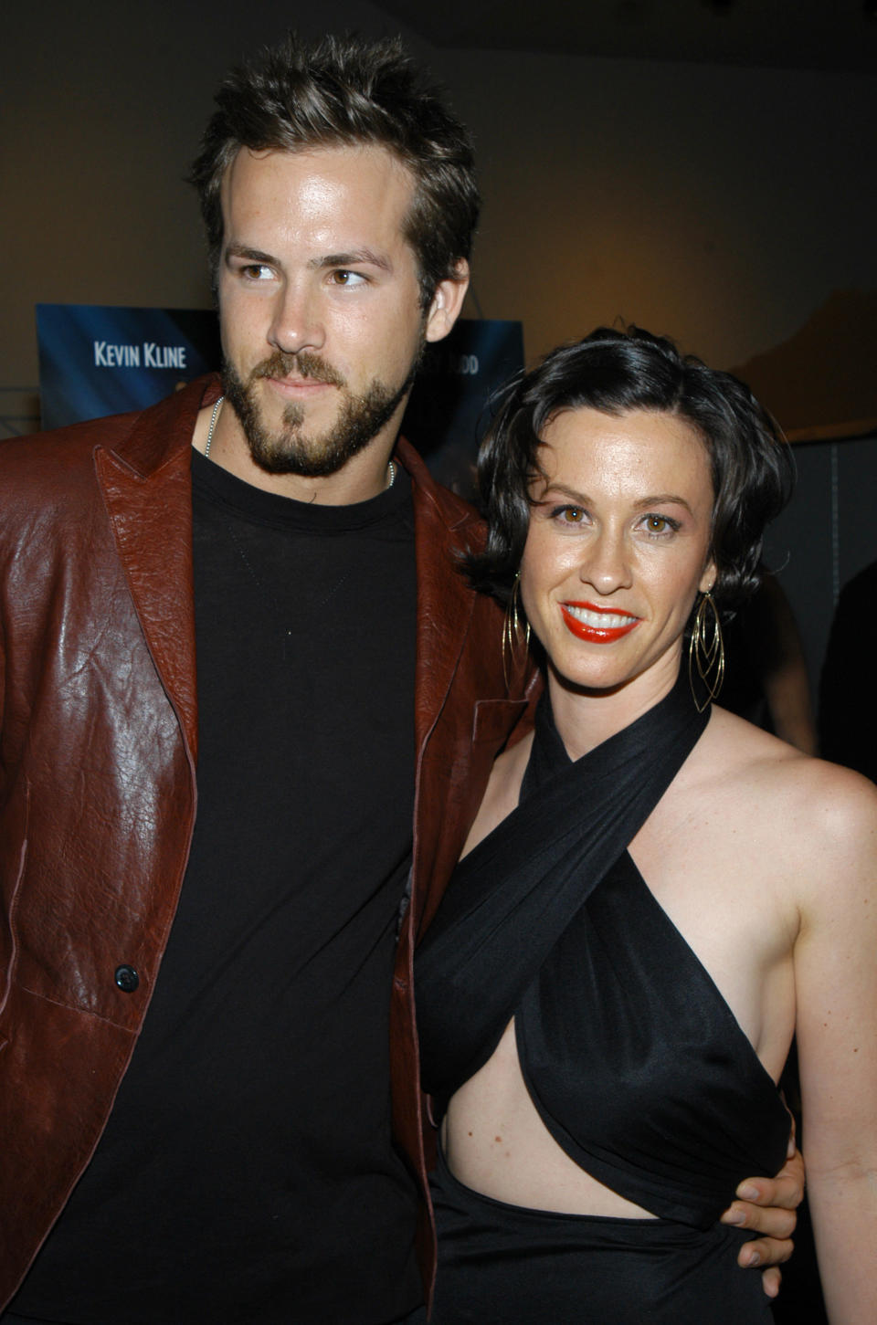 Ryan Reynolds wearing a leather jacket as he stands with his arm around Alanis Morissette, who's wearing a halter top at a premiere