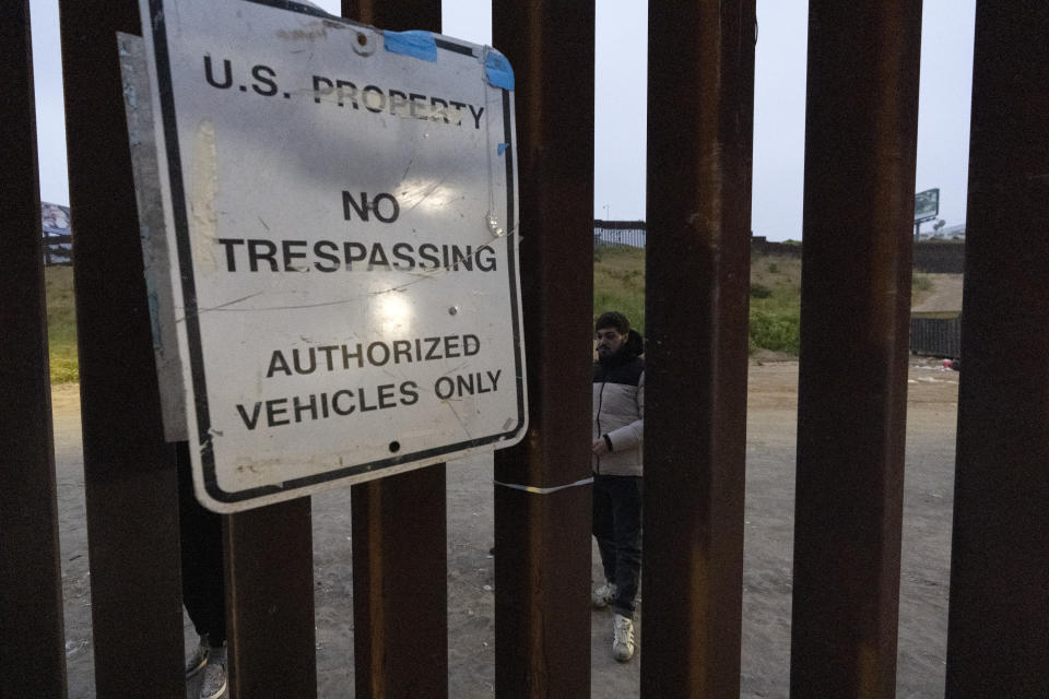 Migrants wait between border walls separating Tijuana, Mexico, and San Diego, to apply for asylum with U.S. authorities, Friday, April 12, 2024, seen from San Diego. (AP Photo/Gregory Bull)