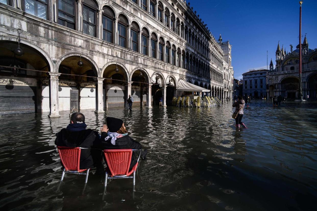 People sit on bistro chairs in the middle of the flooded St. Mark's Square: AFP via Getty Images