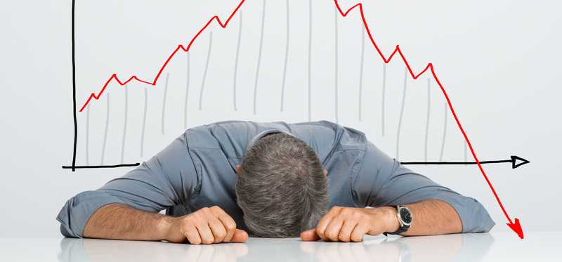 Man has head laid down on table in defeat in front of plunging stock graphs.