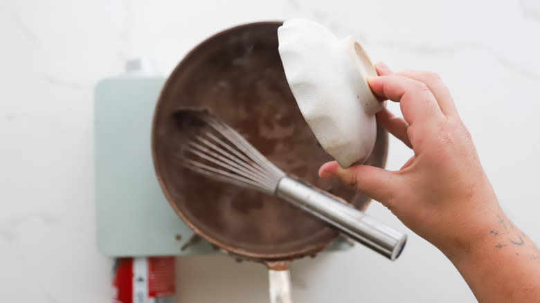 Hand adding chocolate to pot of pudding