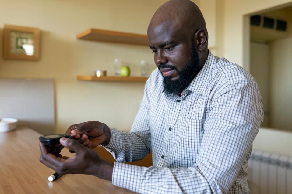 A modern African businessman is sitting at the desk at the home office and is worried about the results of a blood sugar test. The daily life of a man of African-American ethnicity person with a chronic illness who is using glucose tester.