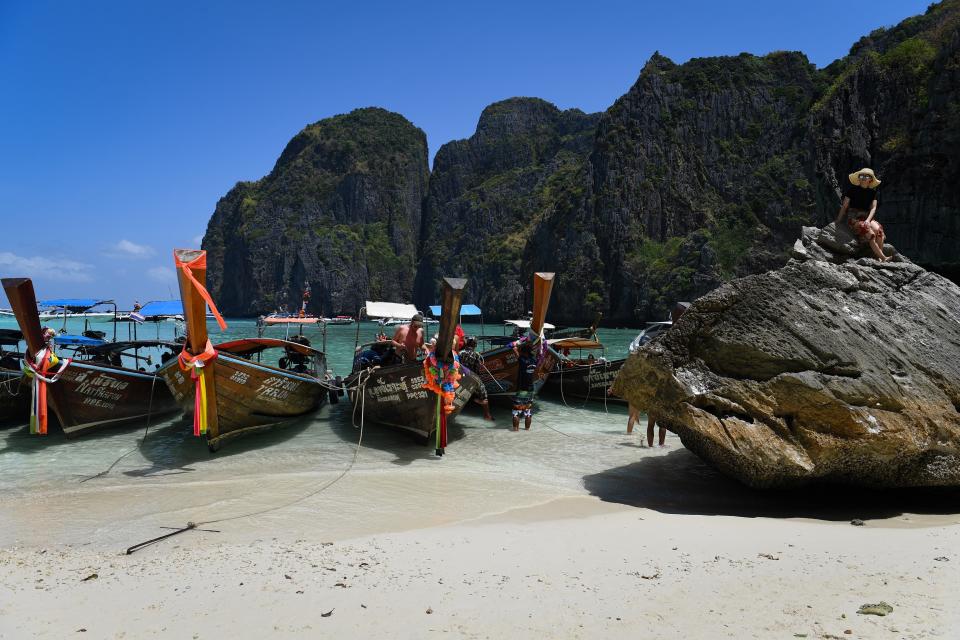 This photo taken on April 9, 2018 shows a tourist sitting on a rock at the edge of Maya Bay on the southern Thai island of Koh Phi Phi.   Across the region, Southeast Asia's once-pristine beaches are reeling from decades of unchecked tourism as governments scramble to confront trash-filled waters and environmental degradation without puncturing a key economic driver. / AFP PHOTO / Lillian SUWANRUMPHA / TO GO WITH AFP STORY "THAILAND-INDONESIA-PHILIPPINES-TOURISM-ENVIRONMENT" by Lillian SUWANRUMPHA with Joe FREEMAN        (Photo credit should read LILLIAN SUWANRUMPHA/AFP/Getty Images)