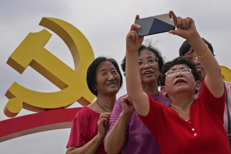 Women take a selfie with a communist party's logo on display at Tiananmen Square to mark the 100th anniversary of the founding of the ruling Chinese Communist Party in Beijing on Monday, July 5, 2021. Chinese leader Xi Jinping on Tuesday attacked calls from some in the U.S. and its allies to limit their dependency on Chinese suppliers and block the sharing of technologies. (AP Photo/Andy Wong)