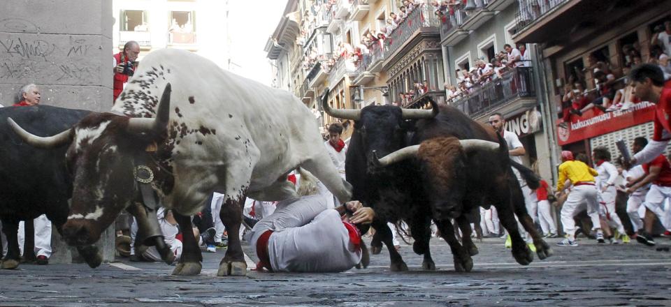 A steer jumps over a fallen runner as two Jandilla fighting bulls follow behind at the Mercaderes curve during the first running of the bulls of the San Fermin festival in Pamplona