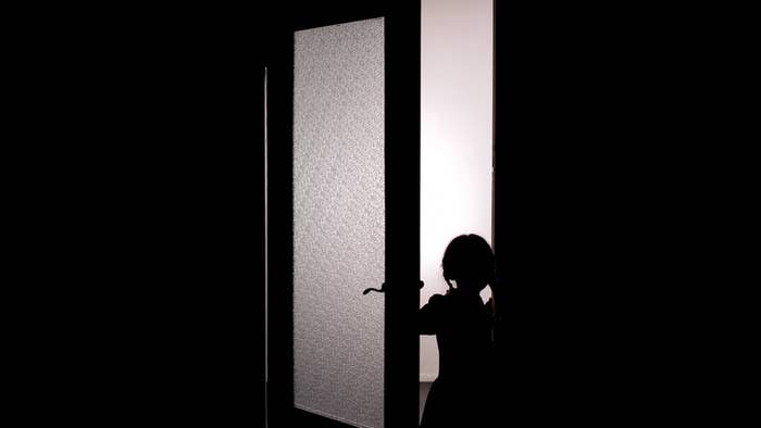 A silhouetted child standing at an open door with light shining from the other side