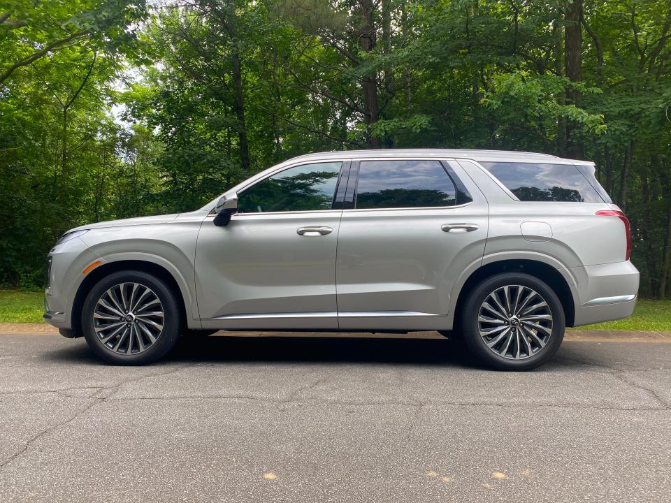 The side view of a silver Hyundai Palisade SUV parked in front of a wooded area